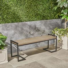 a wooden bench sitting next to potted plants on a stone floor near a wall