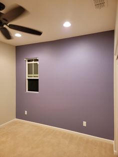 an empty room with purple walls and ceiling fan