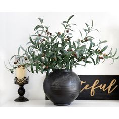 a black vase filled with green plants next to a sign that says beautiful on it