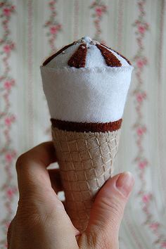 a hand holding an ice cream cone with brown and white decorations on it's top