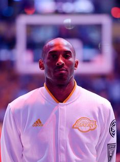 a man standing in front of a basketball hoop wearing a white jacket with gold lettering on it