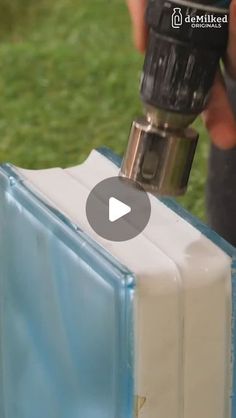 a person using a drill to fix a piece of glass with grass in the background