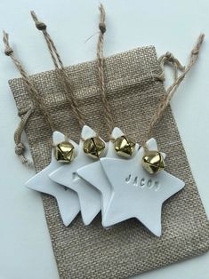 three white ceramic ornaments with gold bells hanging from twine