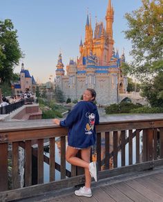 a woman standing on a bridge in front of a castle at disney world with her arms out