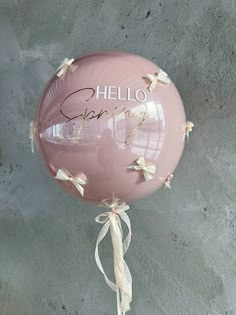 a pink balloon with the word hello grace written on it hanging from a string in front of a gray wall