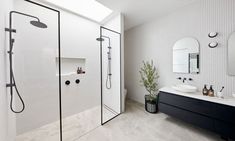 a white bathroom with two sinks and a walk in shower next to a large mirror