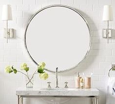 a bathroom vanity with a round mirror above it and flowers on the counter in front of it