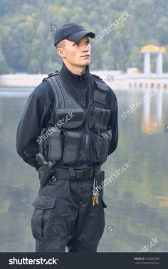 a police officer is standing in front of the water with his hands on his hips