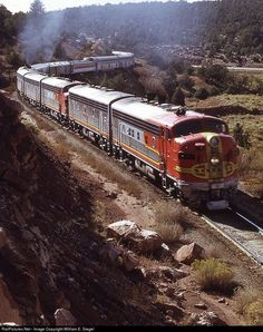 an orange and white train traveling down tracks next to trees on the side of a hill