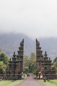 people are walking through an archway in the middle of a park with mountains in the background