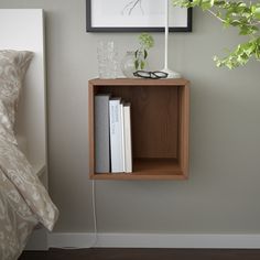 a wooden shelf with books and glasses on it next to a plant in a vase