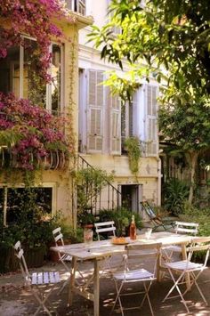 an outdoor table and chairs in front of a building with flowers growing on the windows