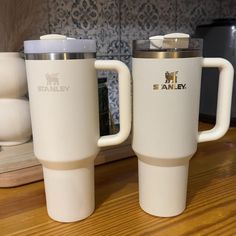 two white coffee mugs sitting on top of a wooden table next to each other