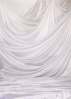 a bed with white sheets on top of it in front of a curtained wall