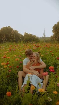 two people sitting in the middle of a field full of flowers and hugging each other