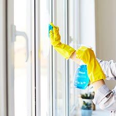 a woman in yellow gloves cleaning windows with a blue bottle and rag on her head