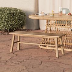 a wicker table and bench sitting on the ground in front of a building with bushes