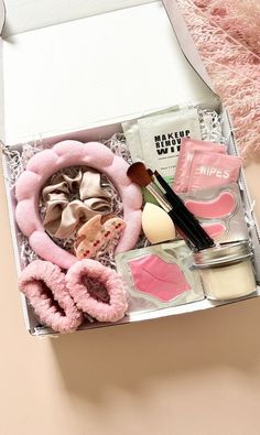 an open box containing makeup and accessories on a pink table cloth next to a teddy bear