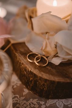 two gold wedding rings sitting on top of a wooden table next to flowers and candles