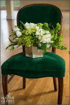 a green chair with flowers and greenery on it sitting in a wood floored room