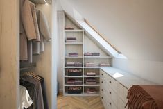 an attic closet with clothes hanging on the shelves and drawers, along with other items