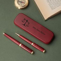 three pens and a pen sitting on top of a desk next to an open book