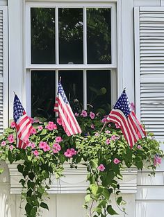 an american flag is hanging from a window sill with pink flowers in the foreground