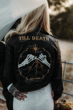 the back of a woman's leather jacket with two hands on it, holding an umbrella