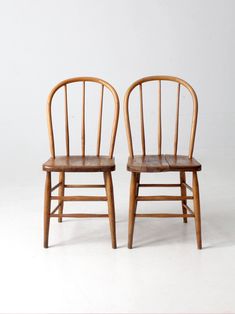 two wooden chairs sitting next to each other on a white surface with one chair facing the other