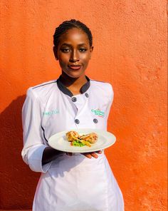 a woman holding a plate with food on it in front of an orange wall,