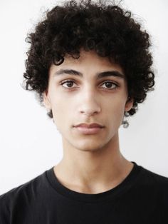 a young man with curly hair wearing a black t - shirt looking at the camera