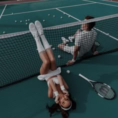 a woman laying on the ground next to a tennis net with two racquets