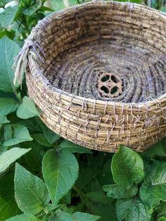 a wicker basket sitting in the middle of some green leaves and bushes with a hole in it