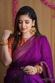 a woman in a purple sari is looking at her cell phone and wearing gold jewelry