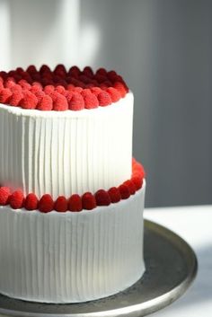 two tiered cake with white frosting and red berries on the top, sitting on a silver platter