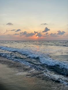 the sun is setting over the ocean with waves crashing on the shore and clouds in the sky