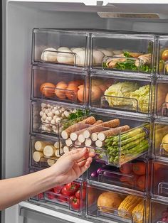 a person reaching into an open refrigerator with lots of food in the bins on it