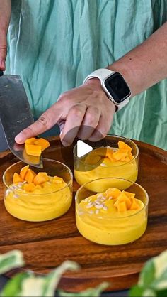 a man is cutting into small desserts on a wooden platter with two glasses