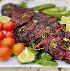 steak, tomatoes and asparagus on a white plate with limes next to it