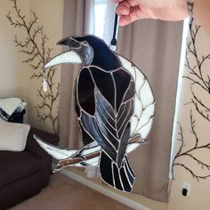 a hand holding a stained glass bird in front of a living room window with curtains