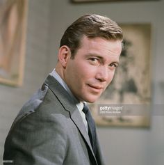 a man in a suit and tie posing for a photo with paintings on the wall behind him