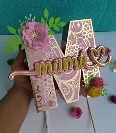 a hand holding up a card with the word mum on it and flowers in front of it