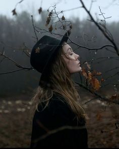 a woman with long hair wearing a black hat and standing in front of a tree