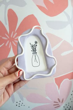 a hand holding a small glass frame with a flower vase on the front and bottom