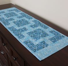 a blue table runner on top of a wooden dresser next to a white wall and brown drawers