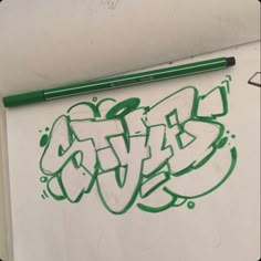 a piece of paper with green graffiti on it next to a marker and pencils