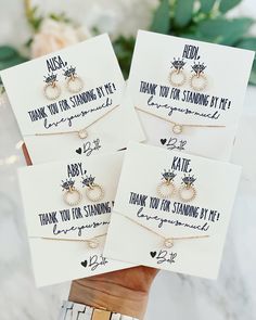 four cards with wedding rings on them are being held by someone's hand in front of some flowers