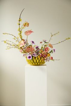 a vase filled with lots of flowers on top of a white table next to a wall