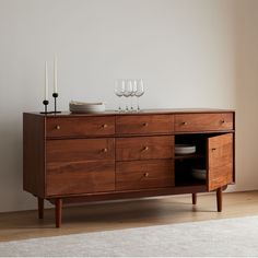 a wooden cabinet with two wine glasses on top and plates in the bottom, next to a white rug