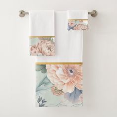 two white towels hanging on a towel rack with flowers and leaves painted on the front